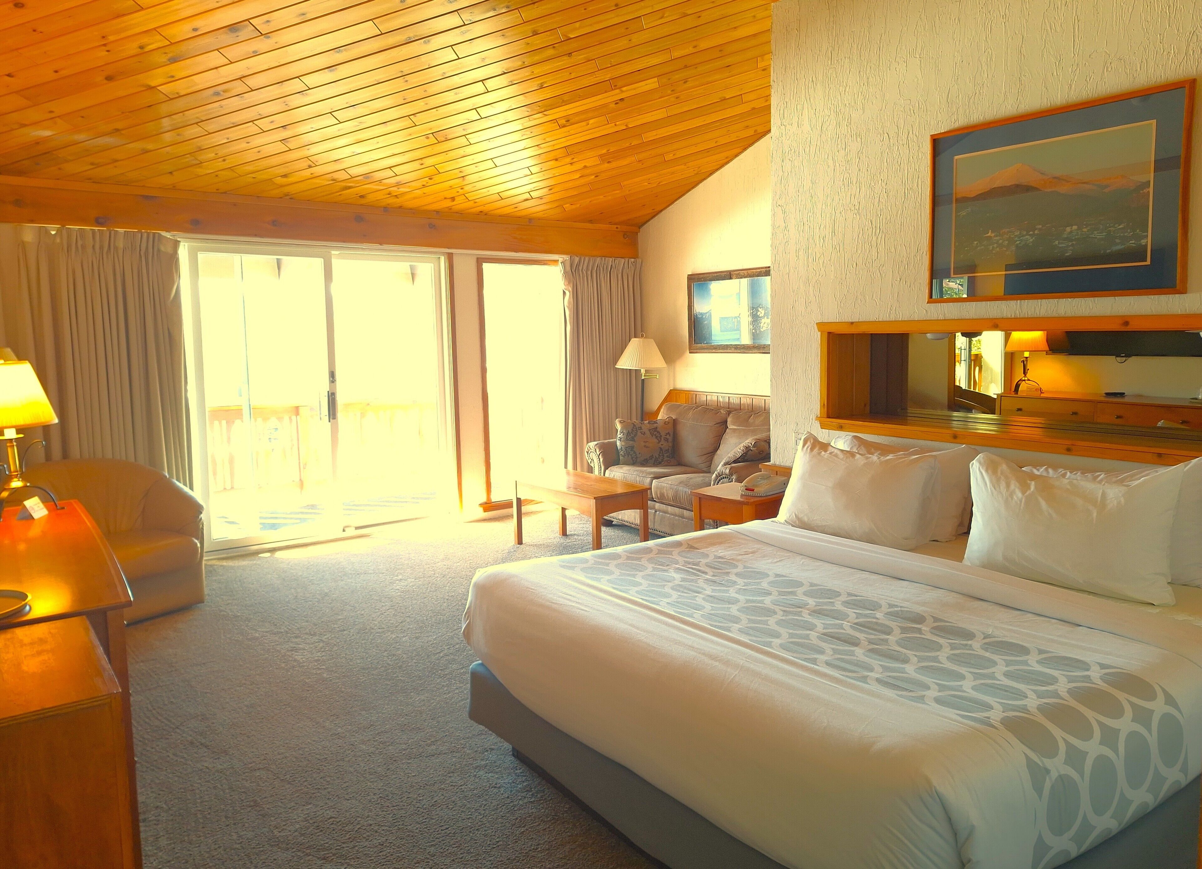 Een hotelkamer met een groot bed, een sofa, een bureau en een balkon met gordijnen.