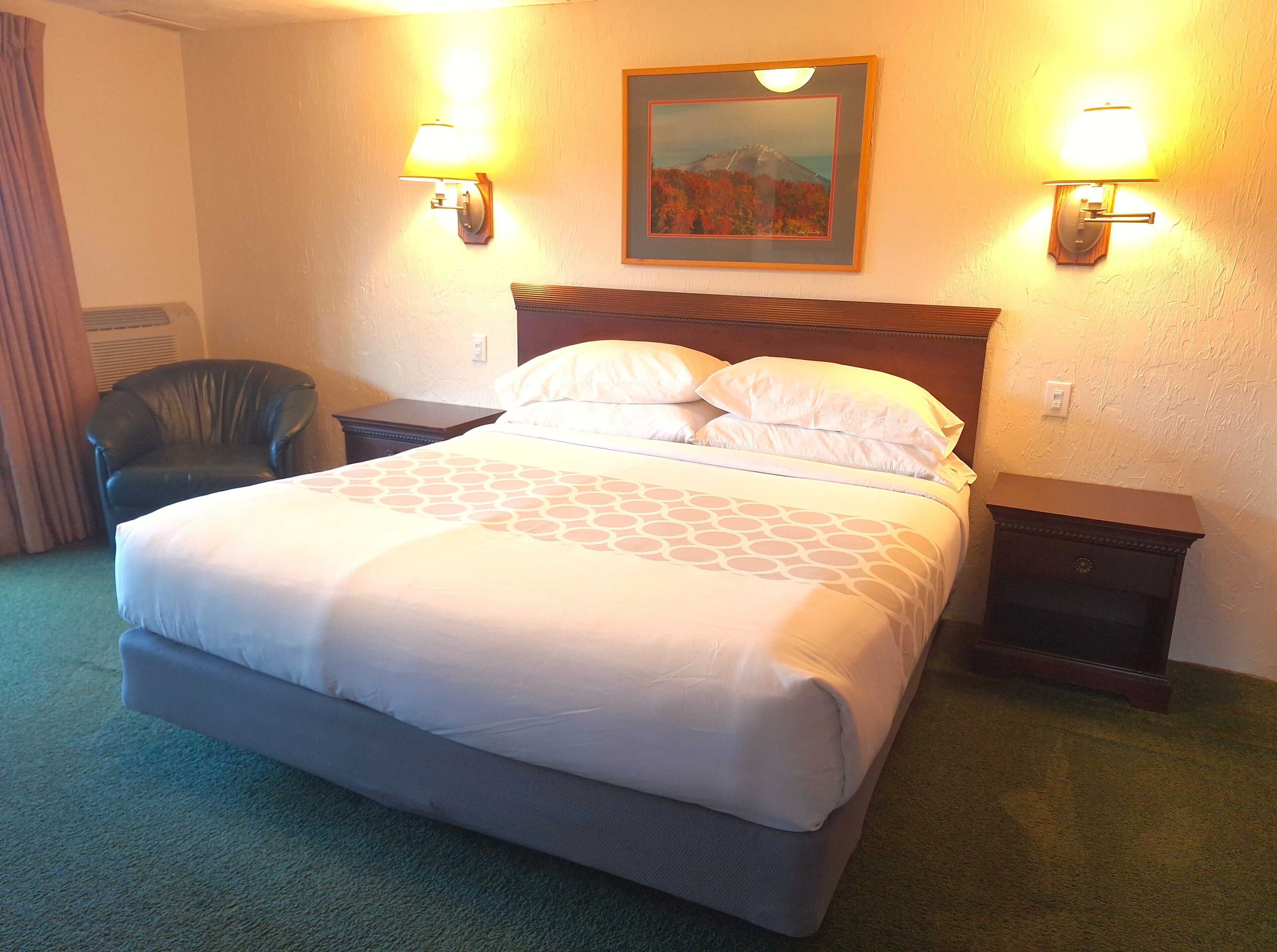 A hotel room with a large bed, two bedside tables, a chair, and two wall-mounted lamps.