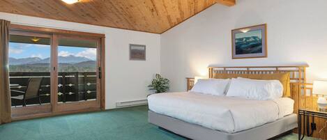 Un dormitorio con una cama grande, techo de madera y vistas a las montañas a través de una puerta corredera.