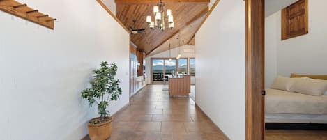 A hallway with a wooden ceiling, a potted plant, and a view to a kitchen area.