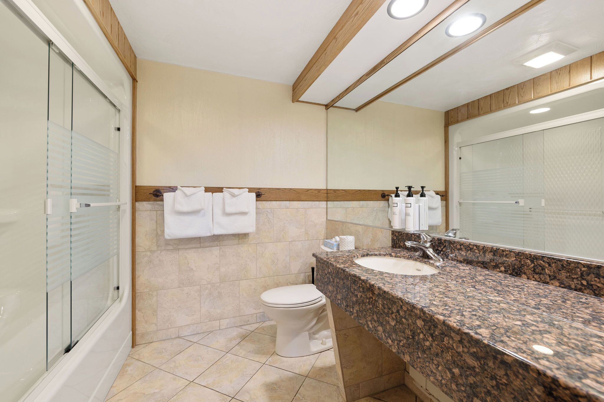 A modern bathroom with a granite countertop, a white toilet, and a glass shower enclosure.
