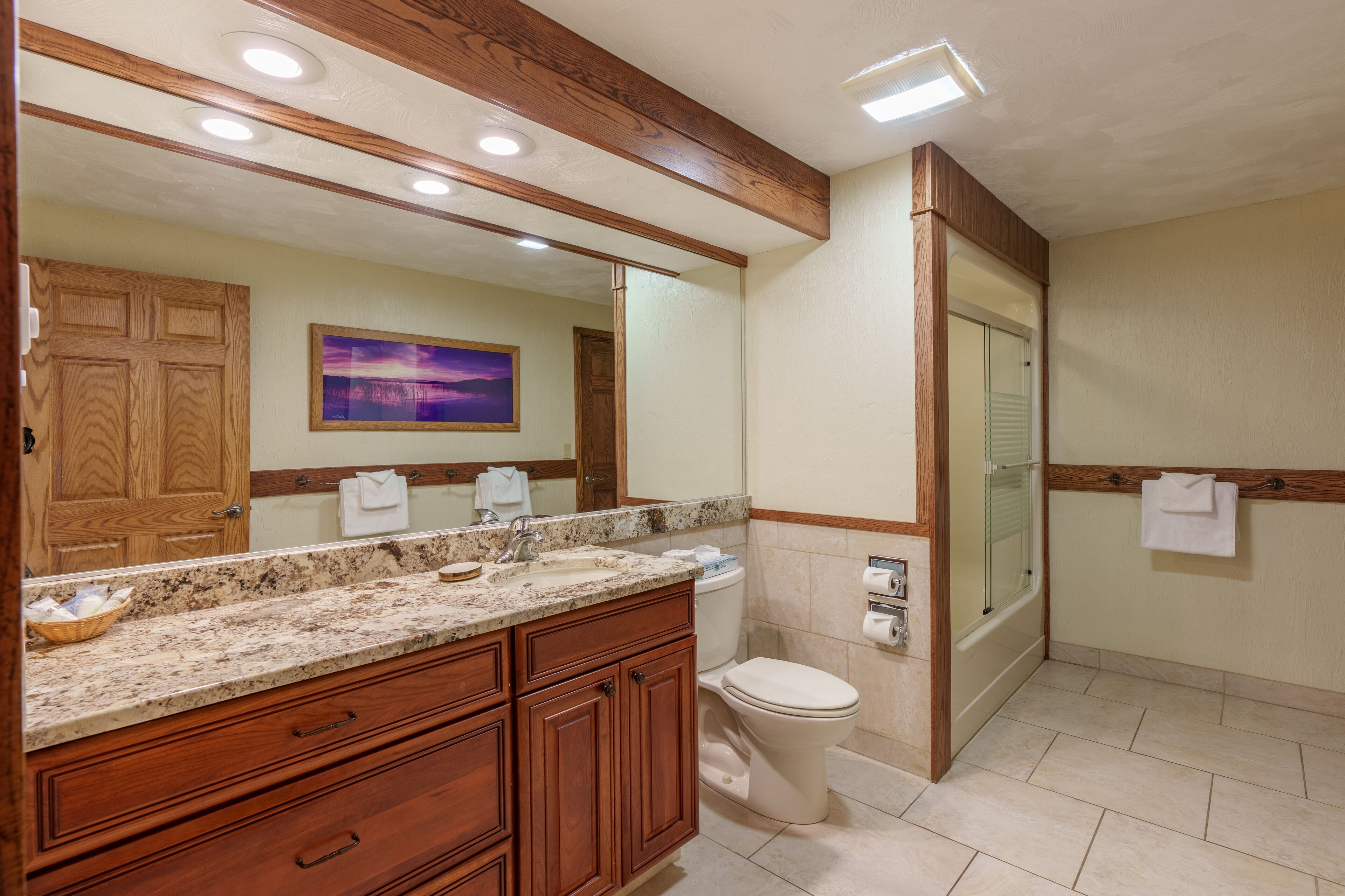A bathroom with a wooden vanity, a large mirror, a toilet, and a shower area.