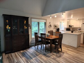 A modern kitchen with a dining area, featuring a large island, dark wooden cabinetry, and a view of the outdoors. - Quiet Cottage in the Woods on the Edge of Town (Hibbing)
