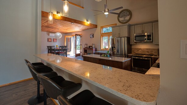Una cocina con una isla grande, taburetes de bar, un ventilador de techo y un reloj en la pared.