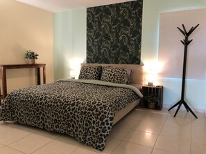 Quarto com cama, duas mesas de cabeceira, uma luminária de chão e parede com padrão de folhas.