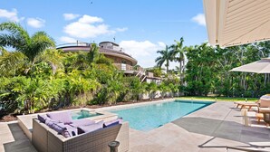 Une piscine avec un jacuzzi, entourée d’une végétation luxuriante et avec un bâtiment moderne en arrière-plan.