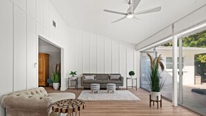 Un salon moderne comprenant un canapé, un fauteuil à capitons, une table basse et une grande fenêtre donnant sur un paysage verdoyant.