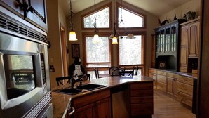 A kitchen with a central island, wooden cabinets, a stainless steel range hood, and pendant lighting.