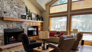 A cozy living room with a stone fireplace, comfortable seating, and large windows.