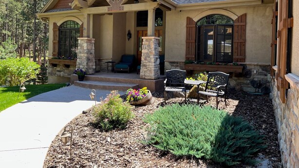 A two-story house with a stone facade, a covered porch with outdoor seating, and a landscaped front yard.