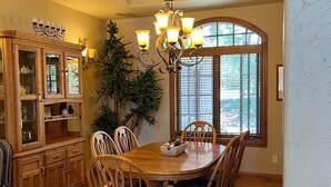 A dining room with a wooden table, chairs, a chandelier, and a large window.
