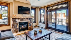 A living room with a stone fireplace, a flat-screen TV, and a ceiling fan. - Luxury 4 Bedroom Condo on Main Street in Downtown Breckenridge (Breckenridge)