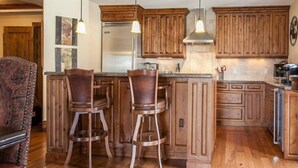 A kitchen with wooden cabinets, a stainless steel refrigerator, and two bar stools. - Vail Arrabelle 3 Bedroom Residence (Vail)