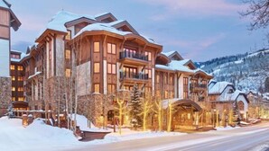 Un gran edificio de varios pisos con techo nevado y varios balcones, rodeado por un paisaje cubierto de nieve.