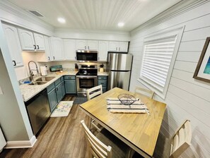 Compact kitchen with a dining table, refrigerator, microwave, oven, sink, and window.