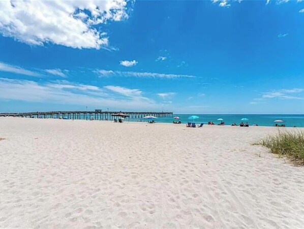 Relax on the beach with comfortable seating and umbrellas, overlooking the calm ocean from the multi-level pier.