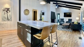 A modern kitchen with a central island, bar stools, and a dining area with a sofa and chairs. - Bear Treehouse - An acre of cool pines, AC, walking distance to fun! (Munds Park)