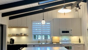 A modern kitchen with a central island, bar stools, and a large window with blinds. - Bear Treehouse - An acre of cool pines, AC, walking distance to fun! (Munds Park)