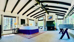 A spacious bedroom with a large bed, a fireplace, and a view of the outdoors. - Bear Treehouse - An acre of cool pines, AC, walking distance to fun! (Munds Park)