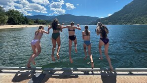 Un groupe de personnes sautant d’un quai dans un lac entouré de montagnes.