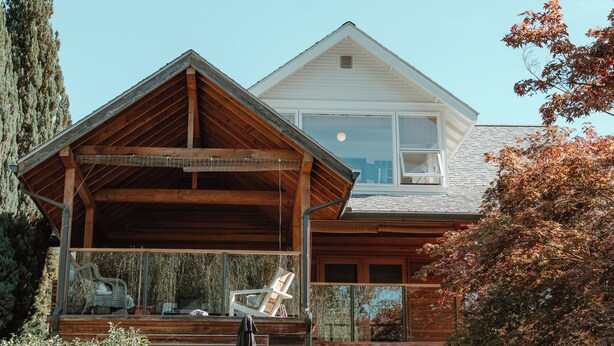 Une maison à deux étages avec une terrasse en bois et un porche couvert.