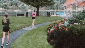 Un sentier dans un parc, avec un grand arbre et, au loin, un bâtiment doté d’un toit rouge.