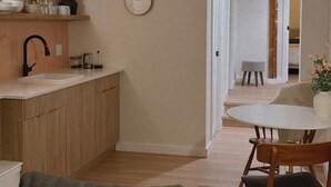 Une cuisine moderne avec des meubles en bois, un évier et une horloge au mur. On y trouve également un coin repas avec une table et des chaises.