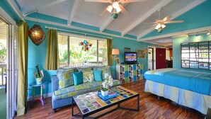 A room with a blue and white color scheme, a sofa, a bed, a television, and a ceiling fan. - Tracy's Tropical Treasure #2 earned "Best in Kihei" four times and “#1 in Maui” (Kihei)