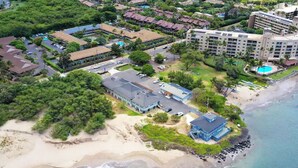 An aerial view of a coastal resort with multiple buildings, a beach, and a swimming pool. - Tracy's Tropical Treasure #2 earned "Best in Kihei" four times and “#1 in Maui” (Kihei)