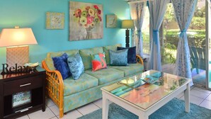 A living room with a sofa, a glass coffee table, and a side table with a lamp. - Tracy's Tropical Treasure #3 earned "Best in Kihei" four times and “#1 in Maui” (Kihei)