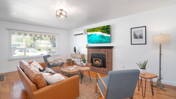 A living room with a fireplace, a television mounted above it, and a large window with blinds.