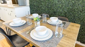 A dining table set with white plates, bowls, and glasses, a small plant centerpiece, and a green wall in the background.
