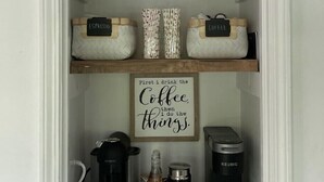 Een koffiebar met planken vol koffiemokken, een bord met daarop de tekst 'Eerst koffie, dan de rest', en apparatuur voor het zetten van koffie.