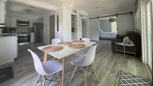 Een moderne keuken met roestvrijstalen apparatuur, een eethoek met een witte tafel en stoelen, en een woongedeelte met een bank en een bed.