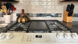 Una cocina con estufa a gas, hervidor y bloque de cuchillos.