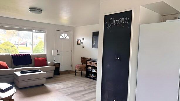 Una sala de estar moderna con un sofá, una mesa de centro y una estantería. Hay una puerta con un cartel que dice "Welcome".