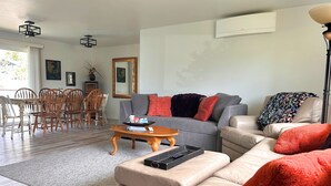 Una sala de estar con un sofá gris, un sofá de cuero color beige, una mesa de comedor de madera y sillas.