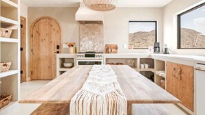 Une cuisine moderne avec une table en bois, un fourneau et une grande fenêtre donnant sur un paysage désertique.