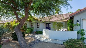 Ein Haus mit Ziegeldach, einer blauen Tür und einem Garten mit einem großen Baum und verschiedenen Pflanzen.