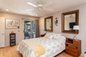 Um quarto com cama, ventoinha no teto, espelho grande, mesa de cabeceira e estante de livros.