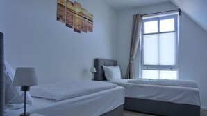 Habitació d'hotel amb dos llits, una taula de nit, una làmpada, una finestra amb cortines i una obra d'art a la paret.
