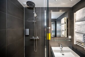 Ein modernes Badezimmer mit einer gläsernen Duschkabine, einem weißen Waschbecken und einem Handtuchhalter.