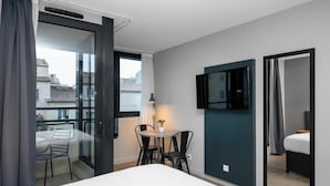 A hotel room with a bed, a small table with two chairs, a TV mounted on the wall, and a balcony with a chair and table. - Staycity Aparthotels Centre Vieux Port (Marseille)