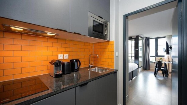 A modern kitchen with grey cabinets, an orange-tiled backsplash, and a stainless steel sink. - Staycity Aparthotels Centre Vieux Port (Marseille)