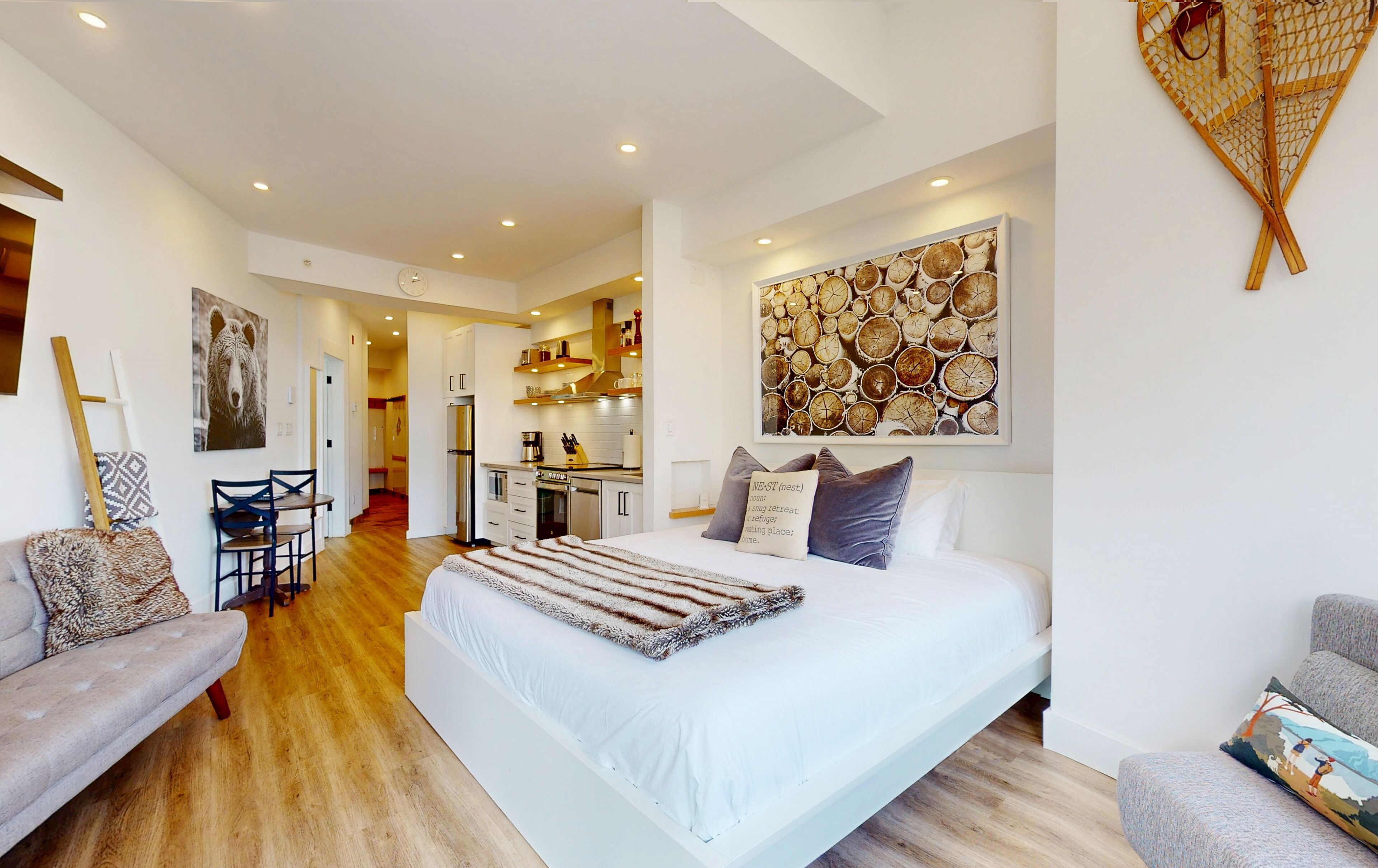 A modern bedroom with a large bed, a dining area, and a kitchen in the background.