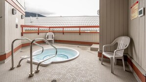 Een dakterras met zwembad, een bubbelbad, twee witte plastic stoelen en een metalen reling.
