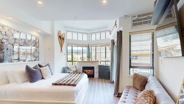 Een moderne slaapkamer met een groot bed, een sofa, een open haard en uitzicht op het landschap.