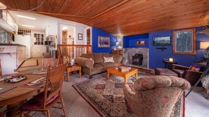 A cozy living room with a wooden ceiling, a blue accent wall, a fireplace, and a dining area with a table and chairs.