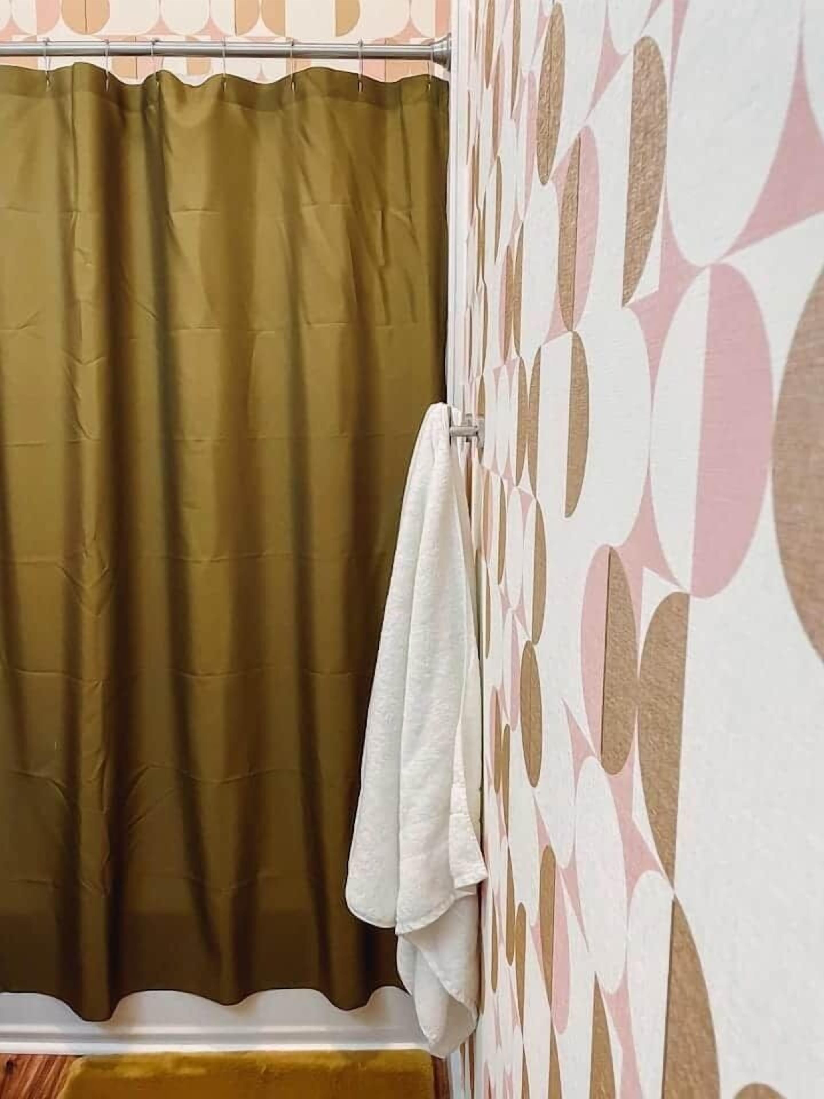 Une salle de bain avec un rideau de douche, une serviette suspendue à un porte-serviettes et un mur décoré d’un motif.