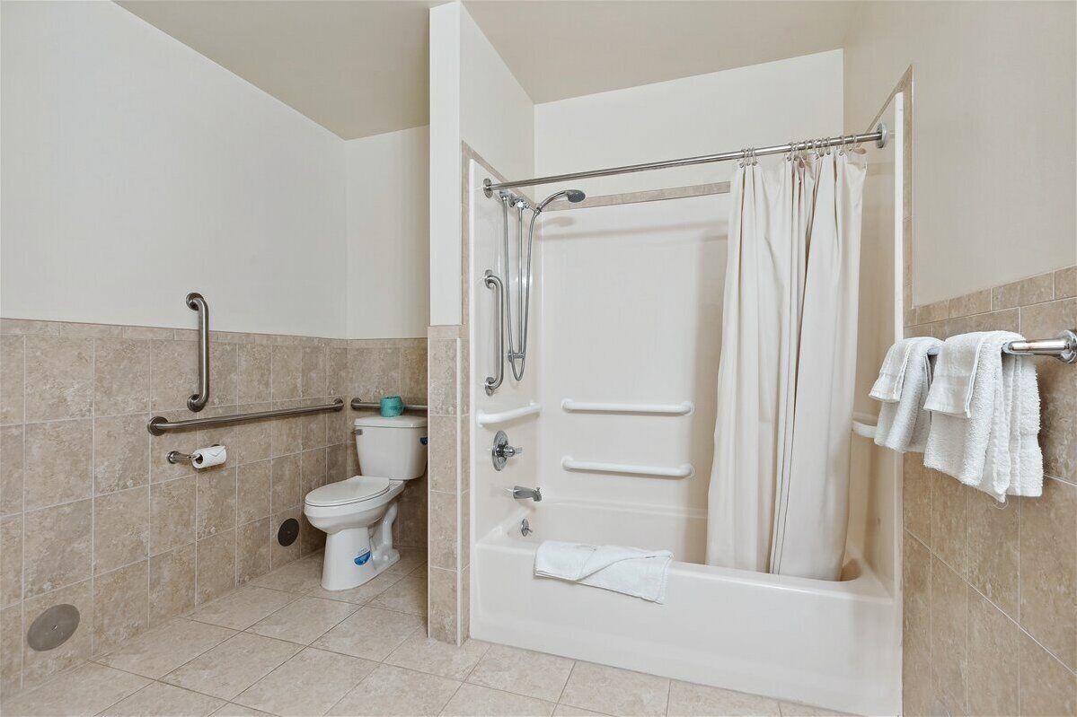 A bathroom with a bathtub, toilet, and handrails.